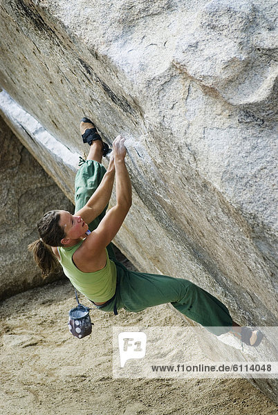 A young woman rock climbs an overhanging face at the Buttermilks near Bishop  California.