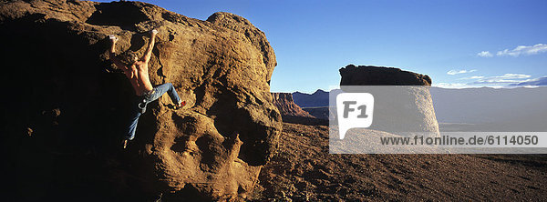 A young man rock climbs a boulder in the desert near Marble Canyon  Arizona.