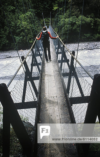 A young woman crosses a suspension bridge over the Tongariro River while Hiking in New Zealand.