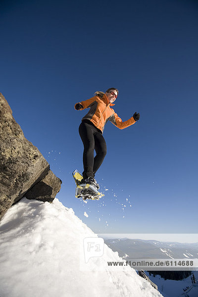 Woman jumps off rock with snowshoes.
