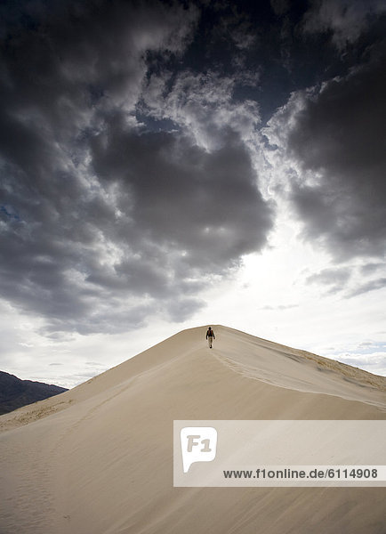 A man walks on natural sand dunes beneath a cloudy sky in Mojave Desert  California.