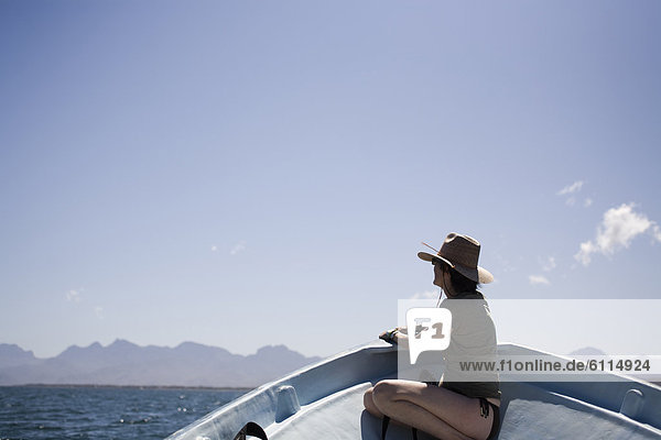A woman sits on the front of a boat with mountains in the distance in Loreto  Baja California Sur  Mexico.