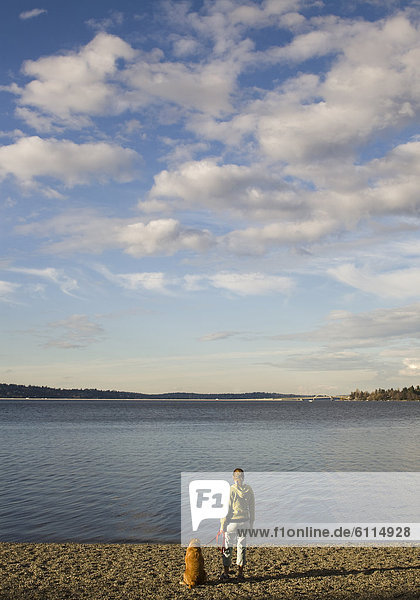 A woman stands on the edge of water with her dog sitting next to her in Seattle  Washington  United States.