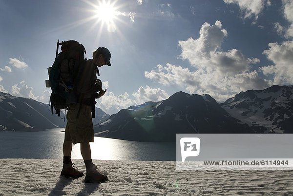 A backpacker stands silhouetted against a dramatic background of the Andes Mountains.