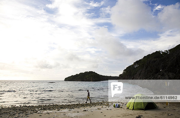 A man walks next to a green tent on an island in the Lau Group in Fiji  South Pacific.