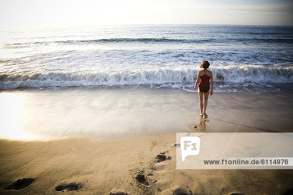 A young woman walks away from the camera into the surf on a quiet beach in Sayulita  Mexico.