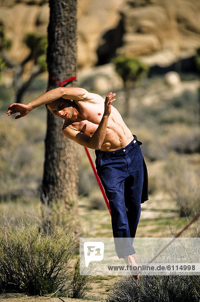 A man uses his arms to maintain balance while tight rope walking or slacklining between two trees in the California desert.
