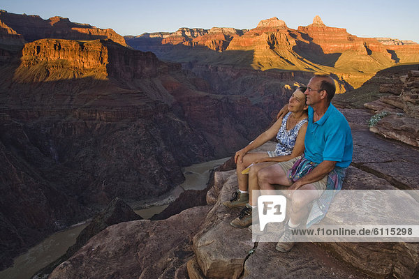 An adult couple sit together looking down at the Colorado River from Plateau Point  Grand Canyon National Park  Arizona.