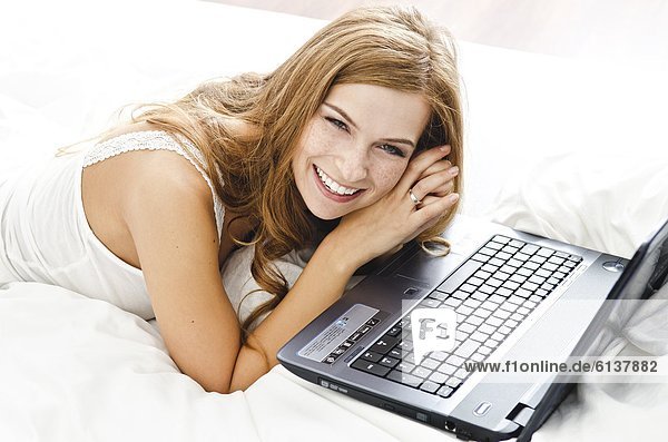 Smiling young woman with laptop in bed