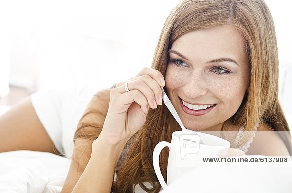 Smiling young woman with cup in bed