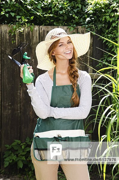 Lächelnde junge Frau mit Sonnenhut und Schürze im Garten
