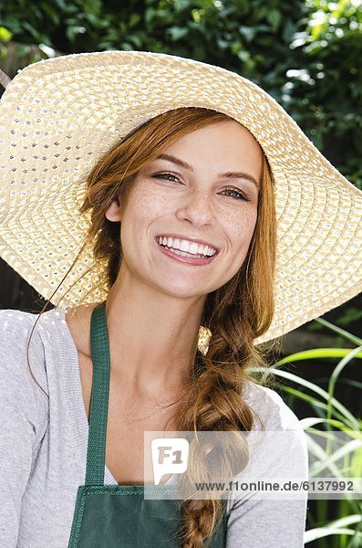 Lächelnde junge Frau mit Sonnenhut und Schürze im Garten  Portrait