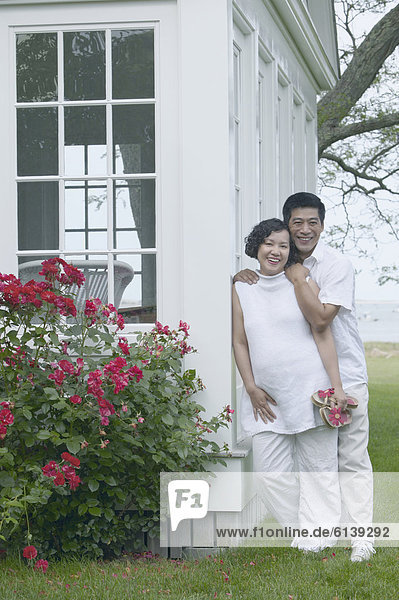 Middle-aged Asian couple leaning exterior of house