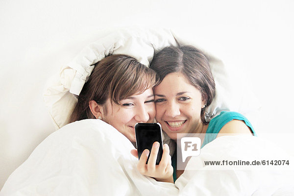 Teenage girls using cell phone in bed