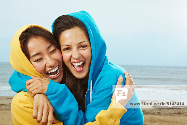 Zwei junge Frauen in Kapuzenoberteilen am Strand