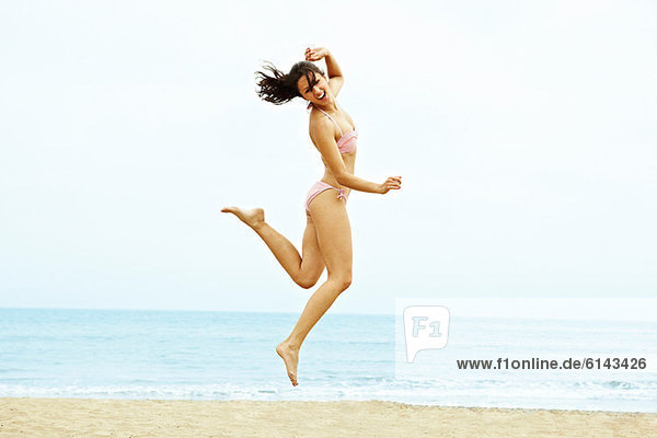 Junge Frau im Bikini beim Springen am Strand