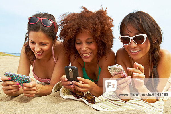 Junge Frauen am Strand mit Mobiltelefonen