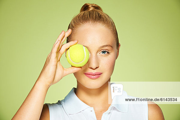 Junge Frau hält Tennisball über das Auge