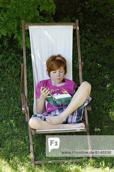 Child  boy  11 years  reading a exciting holiday book whilst sitting in a deck chair in the garden