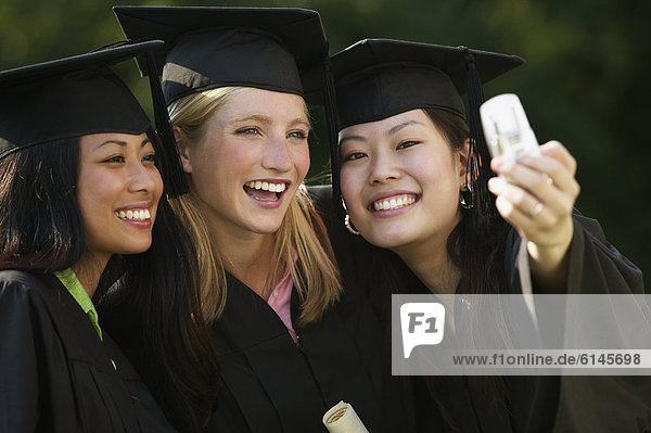 Young women taking pictures of themselves with a camera phone on Graduation Day