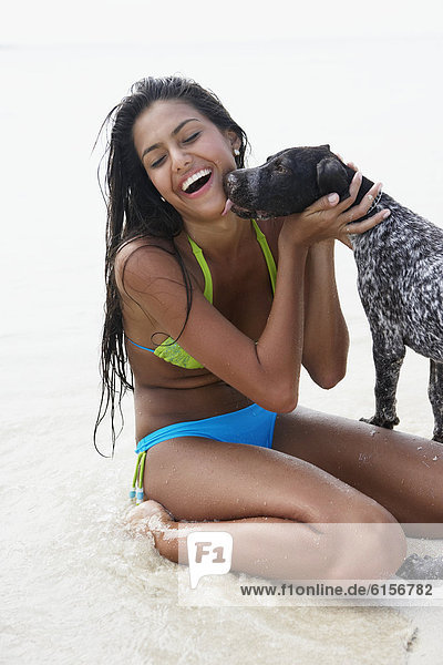 Dog licking South American woman at beach