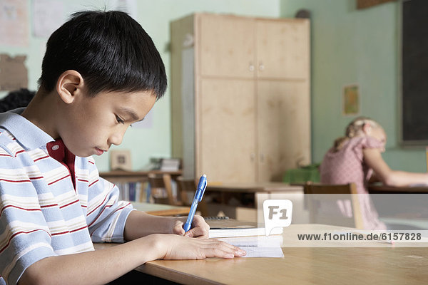 Asian boy writing in classroom