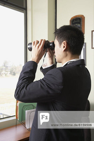 Asian businessman looking through binoculars