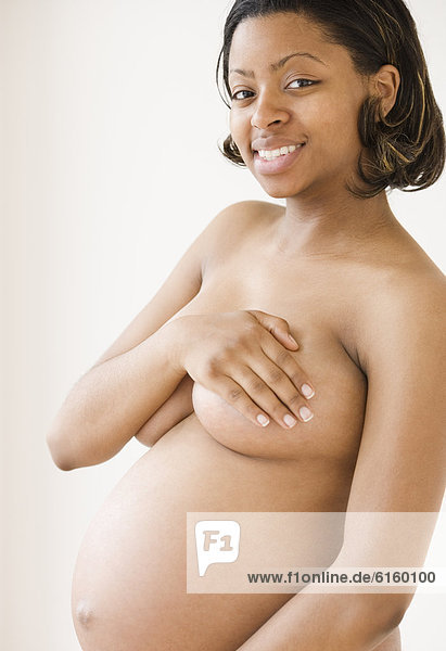 Nude pregnant African American woman covering breasts