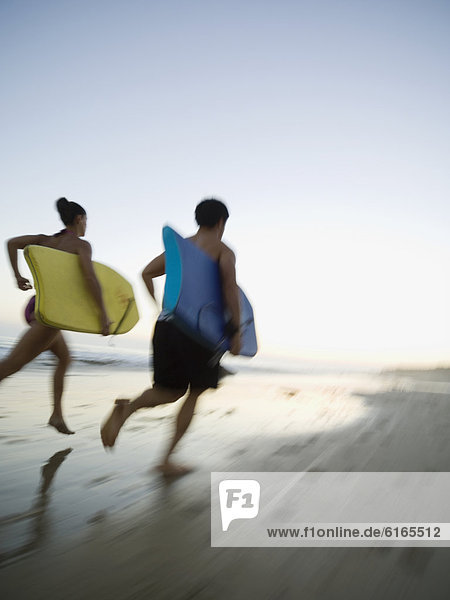 Multi-ethnic couple running with surfboards