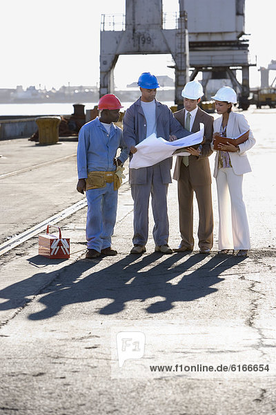 Multi-ethnic businesspeople and construction workers looking at blueprints