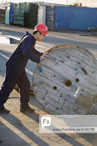 Asian male manual worker pushing wooden spool
