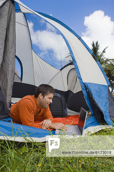 Hispanic man looking at laptop in tent