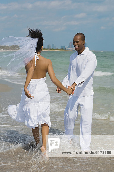 Multi-ethnic bride and groom walking in ocean surf