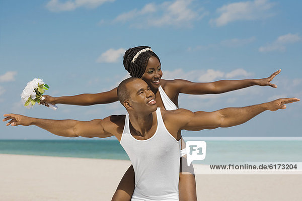 African bride and groom with arms outstretched at beach