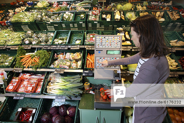 Woman weighing vegetables in the fruit and vegetable section of a self-service grocery department  supermarket  Germany  Europe
