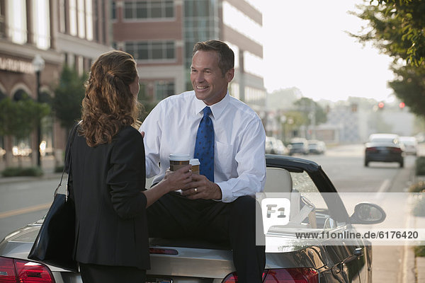 Caucasian businessman sitting on car talking to co-worker
