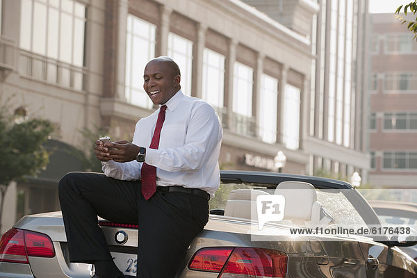 Black businessman text messaging on cell phone outdoors