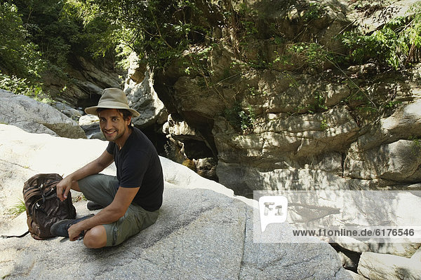 Hispanic man with back pack sitting on rocks
