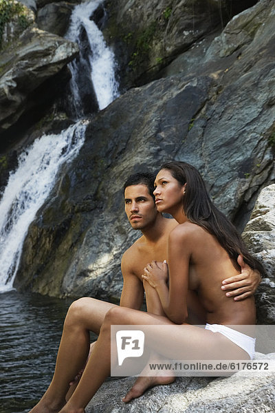 Topless Hispanic couple next to waterfall