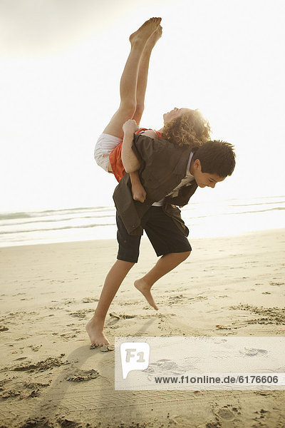 Boy lifting girl on back on beach