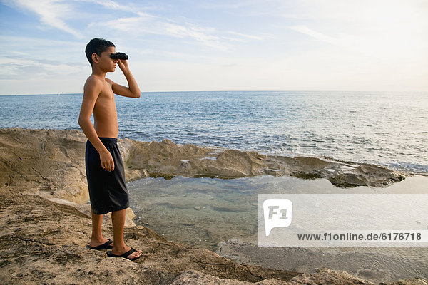 Mixed race boy looking at ocean with binoculars