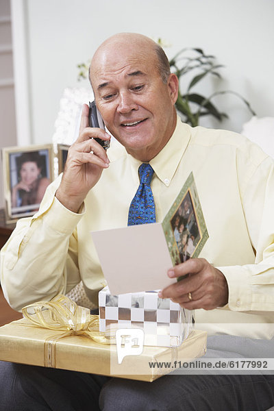 Senior Hispanic man with gifts talking on cell phone