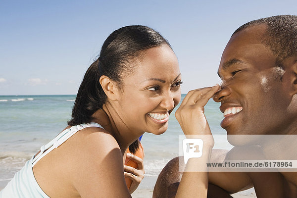 Hispanic woman rubbing sunscreen on boyfriend's nose