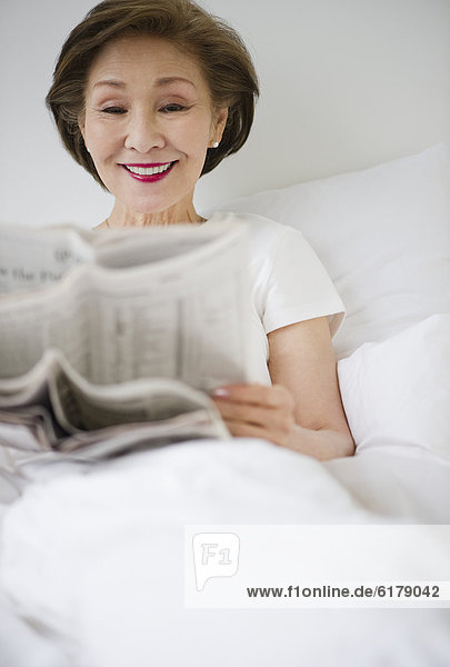 Japanese woman reading newspaper in bed