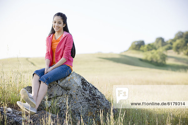 Hispanic girl sitting on rock in field