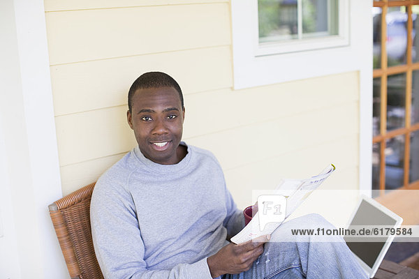Black man on porch reading magazine