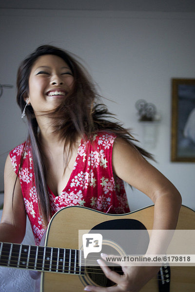 Smiling mixed race teenage girl playing guitar