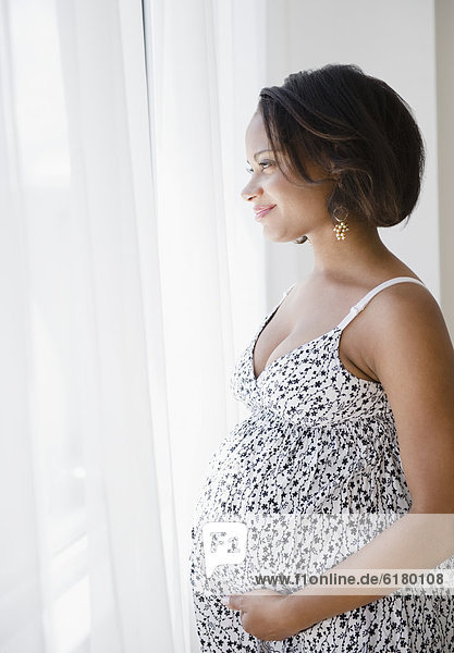 Smiling pregnant Black woman looking out window