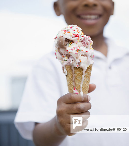 Close up of smiling Black boy holding melting ice cream cone