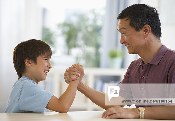 Smiling father and son arm wrestling at table